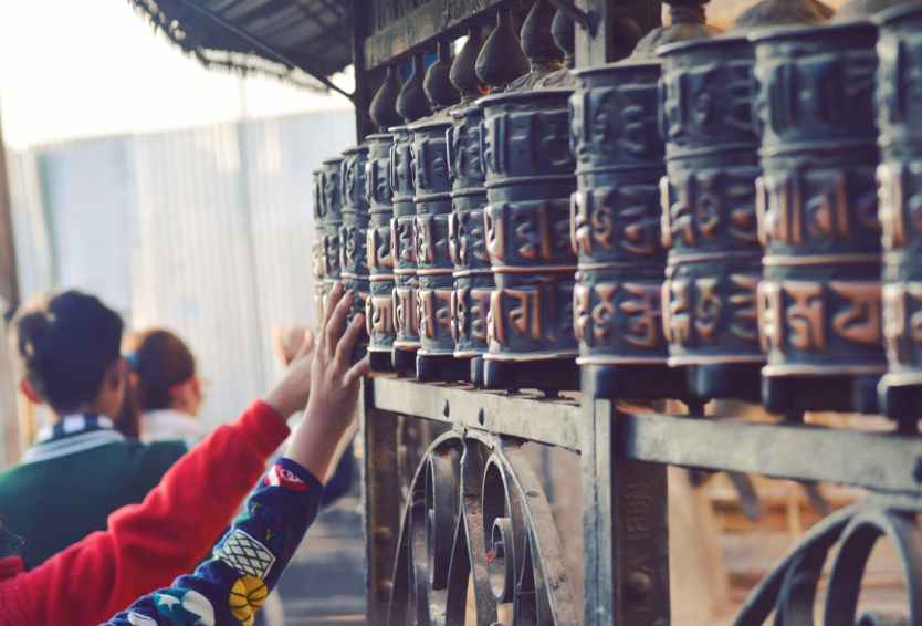 Get Inspired at Swayambhunath (Monkey Temple) 3 unrecognizable pilgrims touching prayer wheels in ancient temple in nepal